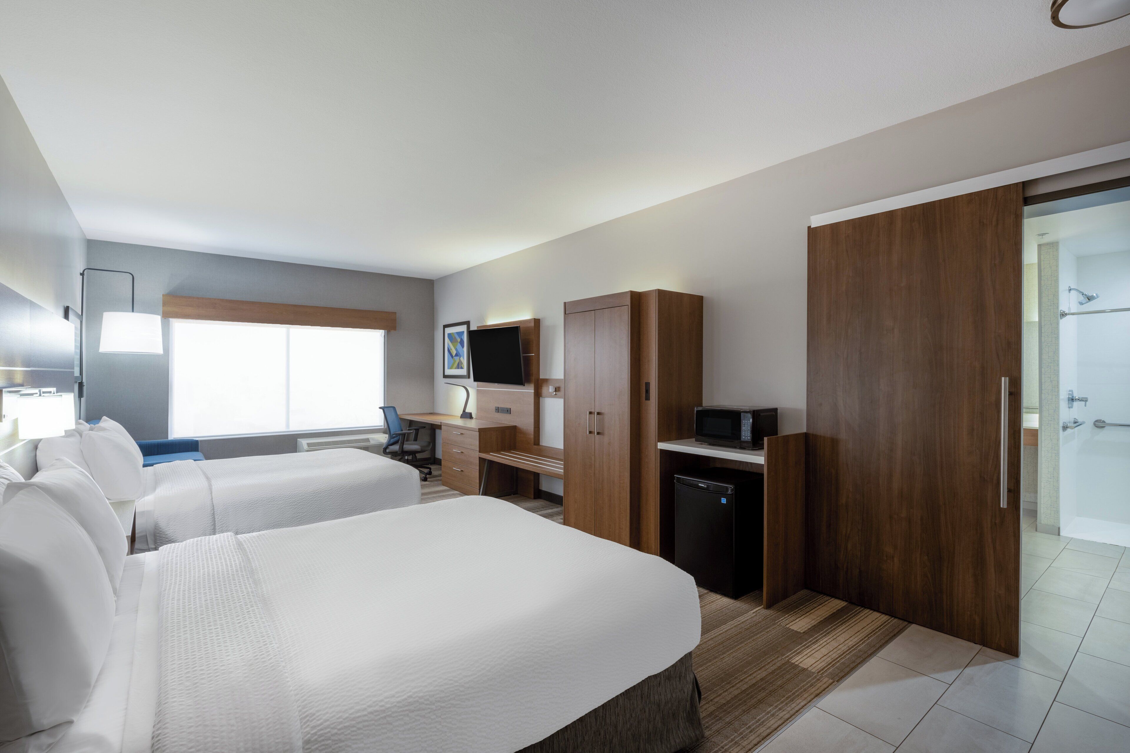 A hotel room with two beds, a desk, a TV, a microwave, and a shower area.