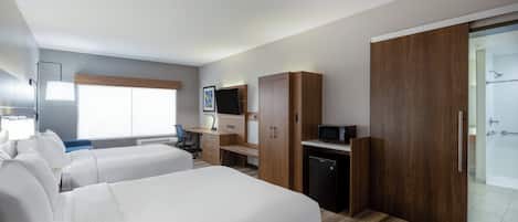 A hotel room with two beds, a desk, a TV, a microwave, and a shower area.