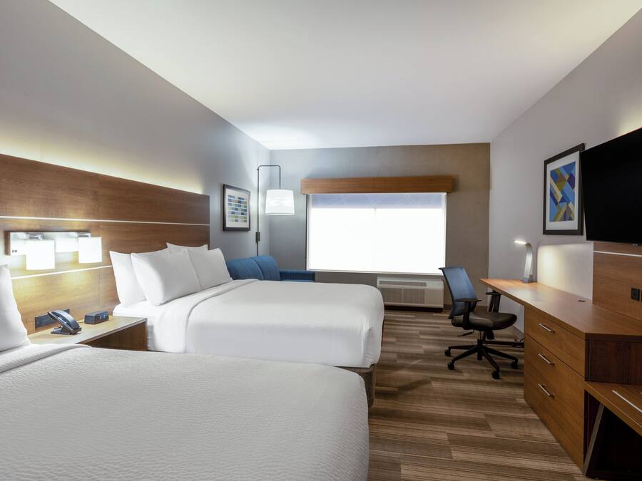 A hotel room with two beds, a desk, a chair, a television, and a window with blinds.