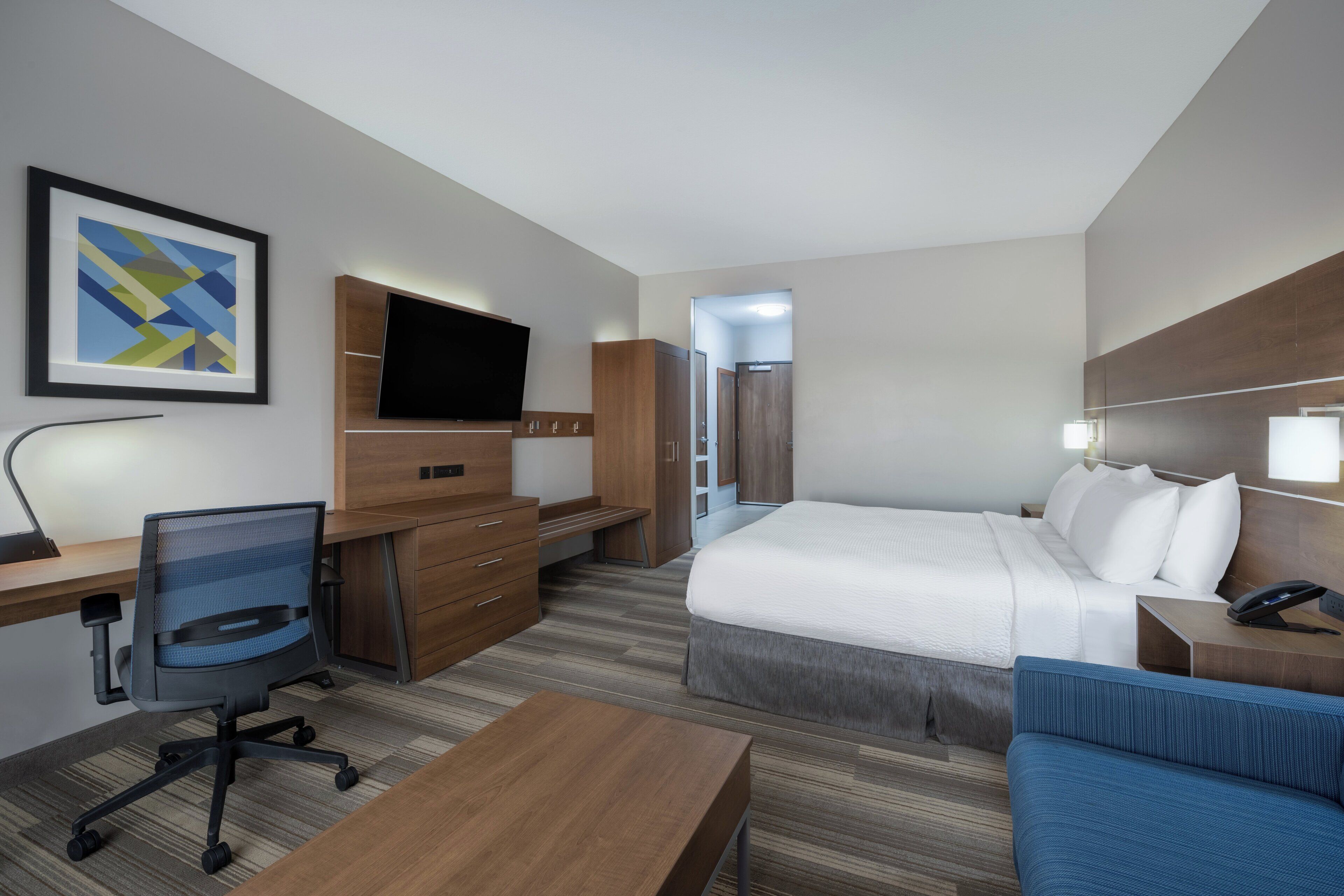 Une chambre d’hôtel moderne équipée d’un lit, d’un bureau, d’une chaise, d’une télévision et d’un tableau encadré au mur.