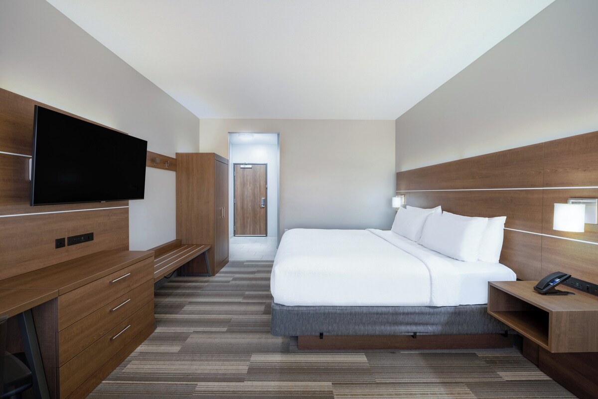 A modern hotel room with a large bed, a flat-screen TV, wooden furniture, and a desk with a phone.