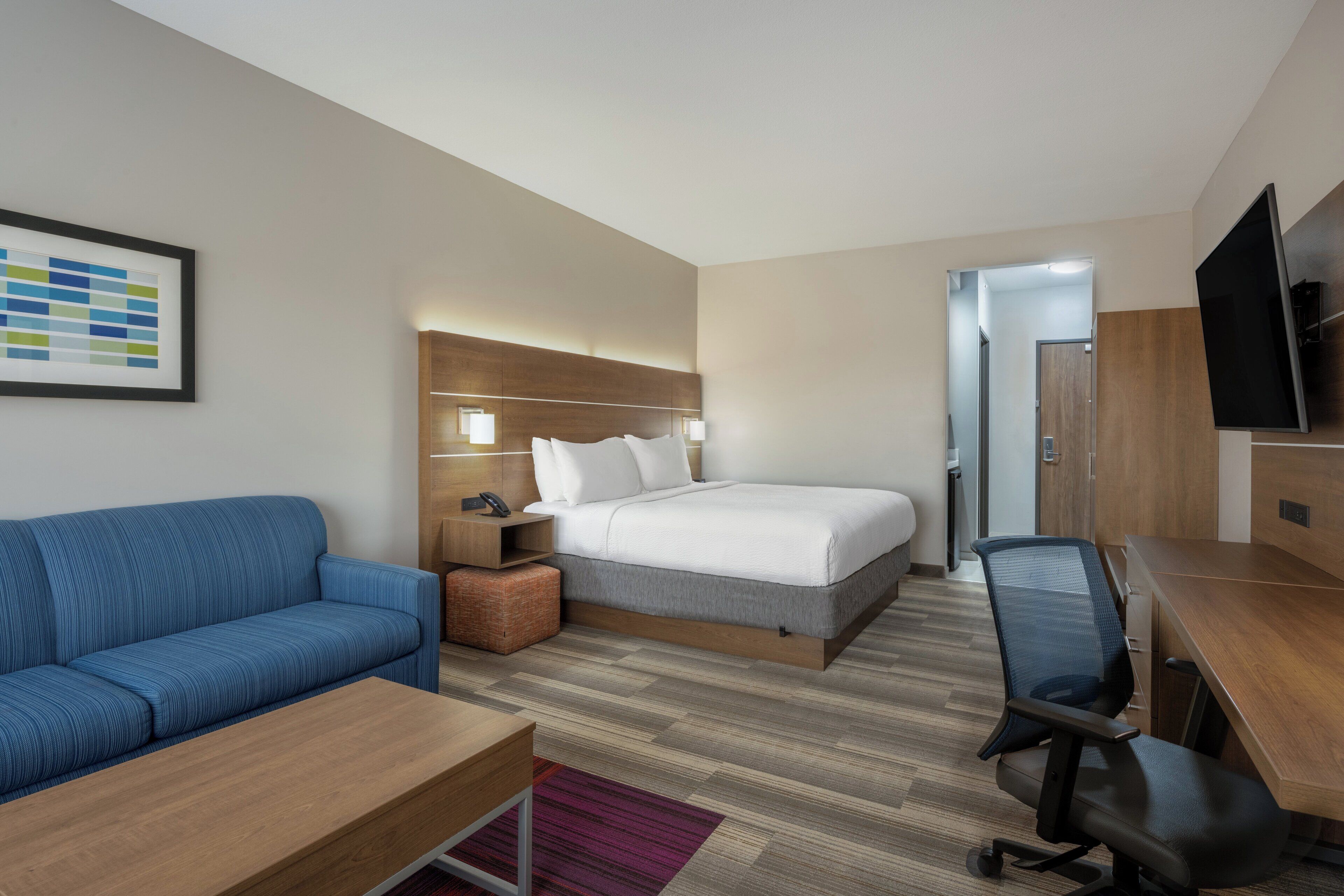 Quarto de hotel com cama, escrivaninha, poltrona, sofá, televisão e mesa de cabeceira.