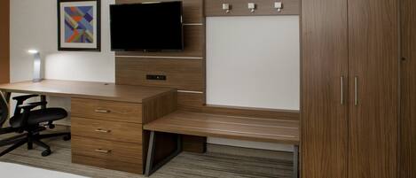 A hotel room with a wooden desk, a flat-screen TV, a bed, and a wardrobe.