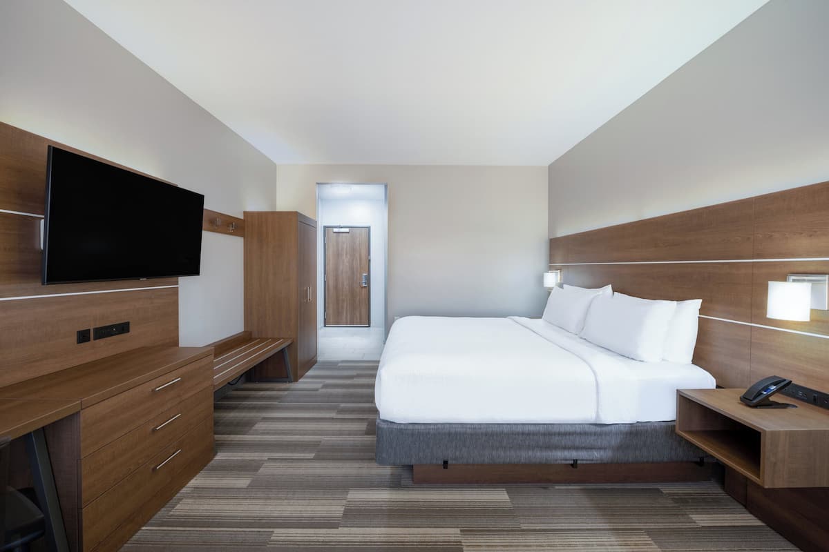 A modern hotel room with a large bed, a flat-screen TV, wooden furniture, and a desk with a phone.