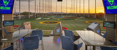 A control room with multiple monitors, chairs, and a view of a golf course at sunset.