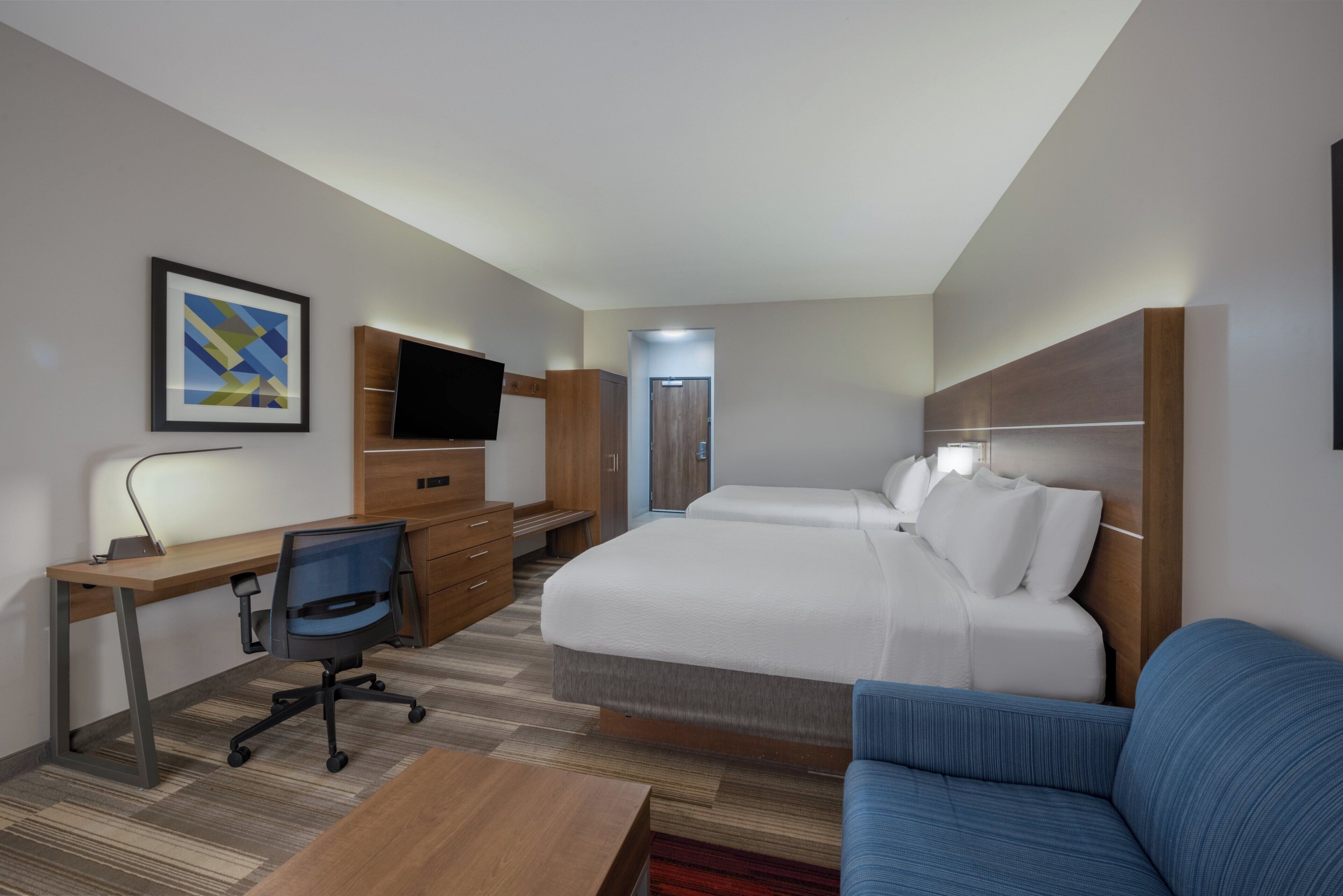 A hotel room with a bed, a desk with a chair, a TV, and a blue sofa.