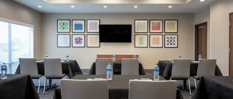 A conference room with tables, chairs, a flat-screen TV, and framed patterns on the wall.