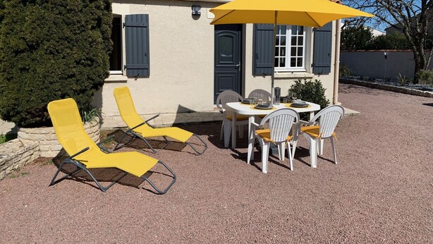 Eine Terrasse mit Tisch und Stühlen, einem gelben Sonnenschirm und einem kleinen Gebäude mit Fensterläden.