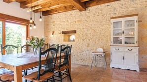 A dining area with a wooden table and chairs, a stone wall, and a cabinet with glass doors.
