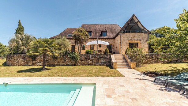 Una casa de piedra con piscina, una escalera de piedra y un jardín.