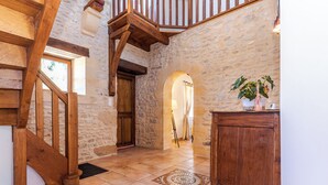 Interior de paredes de piedra con una escalera de madera, una puerta y un mueble pequeño.