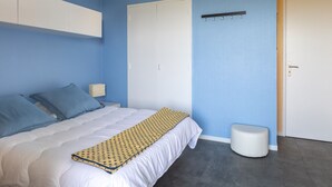 A bedroom with a bed, a white wardrobe, a small bedside table, and a white bench. - T2 Apartment Biscarrosse - AC, Parking, 4 guests, City Center (Biscarrosse Plage)