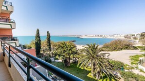 Un balcon avec vue sur la mer, des palmiers et un paysage urbain lointain.