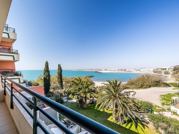 Ein Balkon mit Blick auf das Meer, Palmen und eine ferne Skyline.