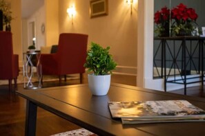 A hotel lobby with a wooden reception desk, a potted plant, red chairs, and a magazine on the desk. - Mins to ASU & Downtown- Foxy on Felder (Montgomery)
