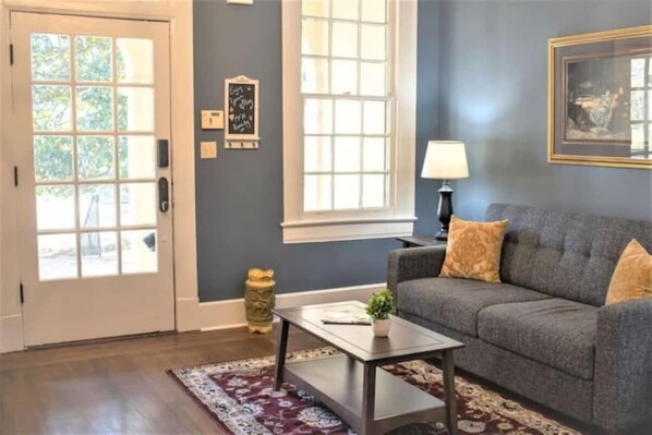 A living room with a grey sofa, a coffee table, a lamp, and a window with blinds. - Mins to ASU & Downtown- Foxy on Felder (Montgomery)