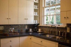 A kitchen with white cabinets, a black countertop, a window with a view of greenery, and a coffee maker. - Mins to ASU & Downtown- Foxy on Felder (Montgomery)