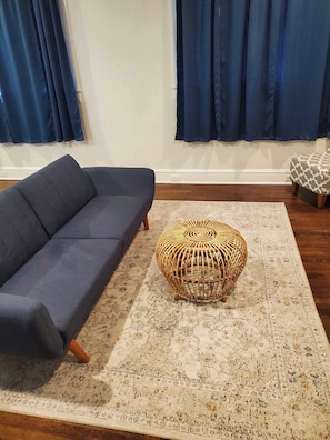 A living room with a dark-colored sofa, a patterned rug, and a woven ottoman. - Mins to ASU & Downtown- Foxy on Felder (Montgomery)