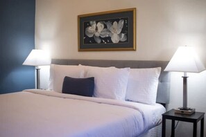 A neatly made bed with white linens and a dark pillow, flanked by two bedside lamps on black nightstands. A framed floral artwork is centered above the bed. - Mins to ASU & Downtown- Foxy on Felder (Montgomery)