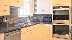 A kitchen with white cabinets, a black countertop, a stove, a microwave, and two ovens.