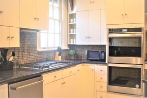 Una cocina con gabinetes blancos, encimera negra, estufa, microondas y dos hornos.