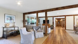 Ein großzügiger Wohnbereich mit Holzboden, zwei grauen Sesseln, einem gestreiften Sofa und einem Couchtisch aus Holz.