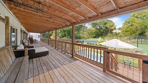 Eine Holterrasse mit Sitzgelegenheiten im Freien, Blick auf ein Schwimmbecken und ein Tennisplatz im Hintergrund.