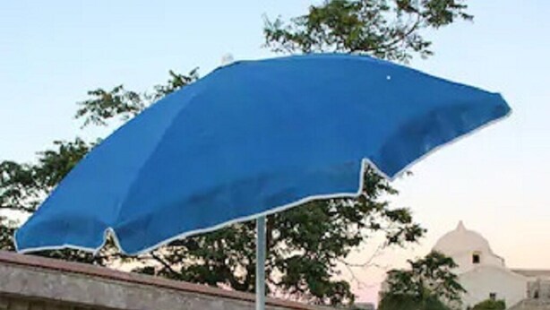 Ein Tisch und zwei Stühle unter einem blauen Sonnenschirm auf einer Dachterrasse.