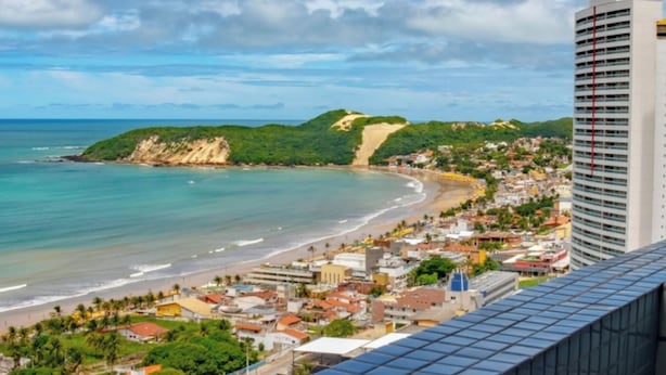 A coastal cityscape with a prominent hotel building, a beach, and a hilly landscape. - Dune& Ocean Views Paradise 2 Beds in Natal (Natal)