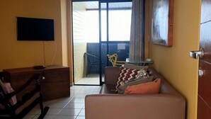 A living room with a sofa, a wooden bench, a TV mounted on the wall, and a sliding glass door leading to an outdoor area. - Dune& Ocean Views Paradise 2 Beds in Natal (Natal)