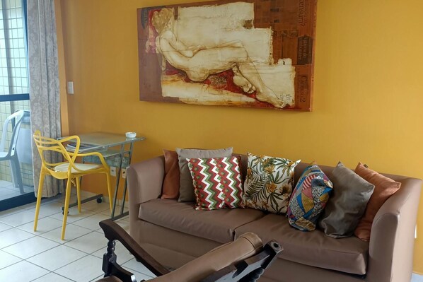 A living room with a brown sofa, colorful cushions, a yellow chair, and a large abstract painting on the wall. - Dune& Ocean Views Paradise 2 Beds in Natal (Natal)