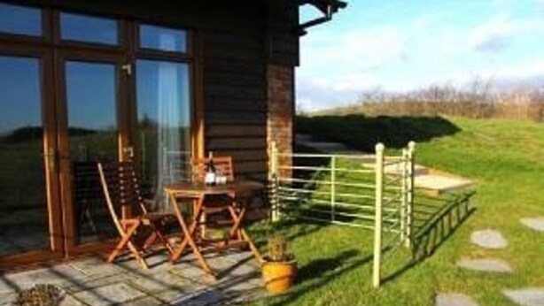 A wooden cabin with a patio area featuring a table and chairs, a gate, and a stone pathway. - Poachers Hut 1-bed Cottage, Sleeps 2, Pet Friendly (Newport)
