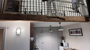A loft-style room with a wooden beam ceiling, a metal railing, and a view of the kitchen below. - Poachers Hut 1-bed Cottage, Sleeps 2, Pet Friendly (Newport)