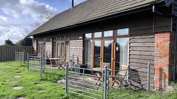 A wooden building with a tiled roof, large windows, and a fenced outdoor area with chairs and tables.
