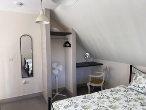 A bedroom with a bed, a desk, a chair, a hanging light, a fan, and a mirror.