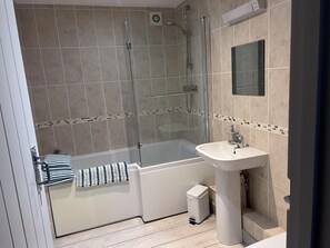 A modern bathroom with a glass-enclosed shower, a white sink, and a tiled floor.