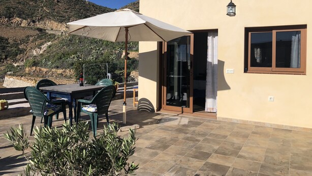 Eine Terrassengruppe im Freien mit Tisch, Stühlen und einem großen Sonnenschirm, mit Blick auf eine Hügelkuppe.