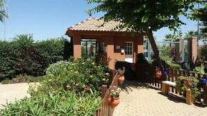 A small, single-story building with a tiled roof, surrounded by a garden with various plants and flowers. - Playa Canela I - Punta del Moral Beach PPHC36P36 (Punta del Moral)