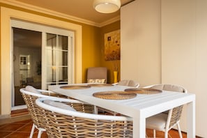 A dining area with a white table and wicker chairs, a glass door entrance, and a painting on the wall. - Playa Canela I - Punta del Moral Beach PPHC36P36 (Punta del Moral)