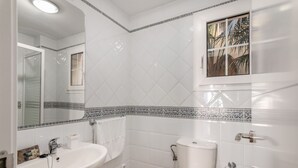 Een badkamer met een wit wastafelmeubel, toilet en een raam met uitzicht op palmbomen.