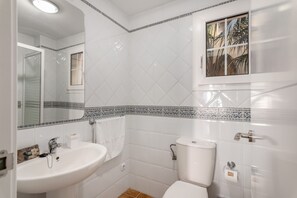 Une salle de bain avec un lavabo blanc, des toilettes et une fenêtre donnant sur des palmiers.
