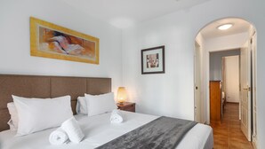 Een hotelkamer met een groot bed, een hoofdbord, een nachtkastje met een lamp, en twee kunstwerken in lijsten aan de muur.