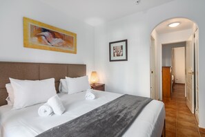 Une chambre d’hôtel avec un grand lit, une tête de lit, une table de chevet avec une lampe et deux œuvres d’art encadrées accrochées au mur.