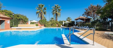 A clear blue pool with a lifeguard stand, surrounded by palm trees and lounge chairs.