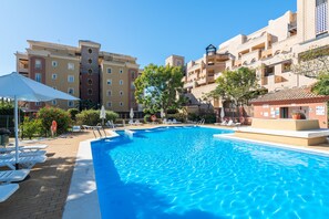 Une piscine entourée de bâtiments à plusieurs étages dotés de balcons, avec des chaises longues et des parasols à proximité.