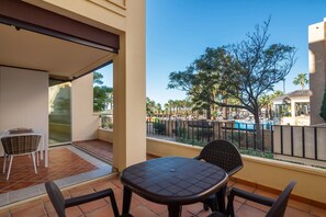 A balcony with a table and chairs, a view of a pool area, and a tree. - Playa Canela I - Punta del Moral Beach PPHC36P36 (Punta del Moral)