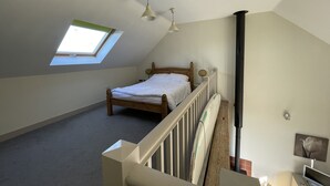 A bedroom with a sloped ceiling, a skylight, a bed, a wooden headboard, a white railing, and a black pipe. - Surf Shack, 1-bed Cottage, Sleeps 2, Pet Friendly (Newport)