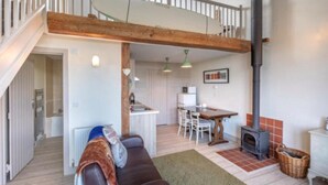 A cozy living room with a brown leather sofa, a dining area with a table and chairs, a kitchen with a stove, and a staircase leading to an upper level. - Surf Shack, 1-bed Cottage, Sleeps 2, Pet Friendly (Newport)