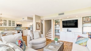 A modern living room with a grey sofa, a coffee table, and a TV mounted on the wall. - Renovated Oceanfront Condo with Ground-Level Patio on Amelia Island (Fernandina Beach)
