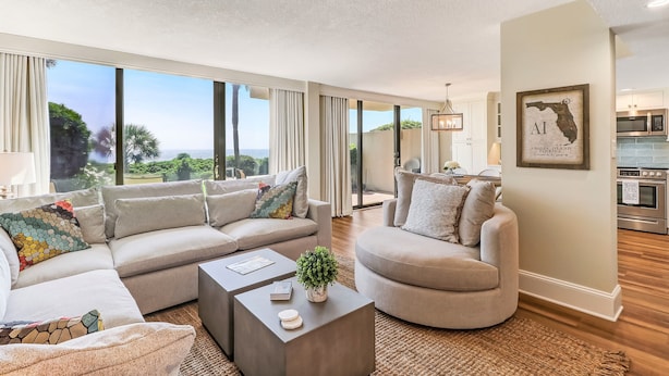 A spacious living room with large windows, a modern kitchen, and a view of the outdoors. - Renovated Oceanfront Condo with Ground-Level Patio on Amelia Island (Fernandina Beach)